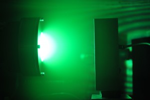 In this photograph of Berkeley Labs system for self-sputtering far above the runaway threshold, neutral excited copper atoms in the plasma glow green while, near the magnetron target, a plentiful supply of ions glows white.